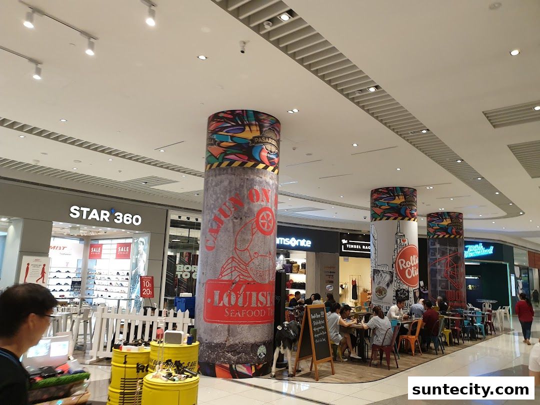 A shopping mall interior with various shops and dining areas, featuring decorative pillars.