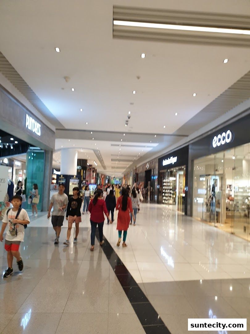People walking in a bright, modern shopping mall with various stores visible.