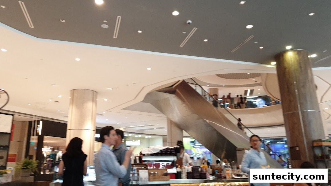 People are seen in a modern shopping mall with escalators and shops.