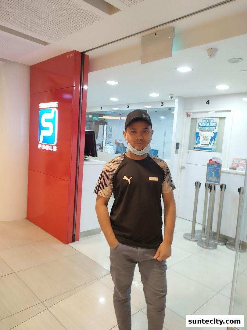 A man stands in front of the Singapore Pools shop entrance with its distinctive red signage.
