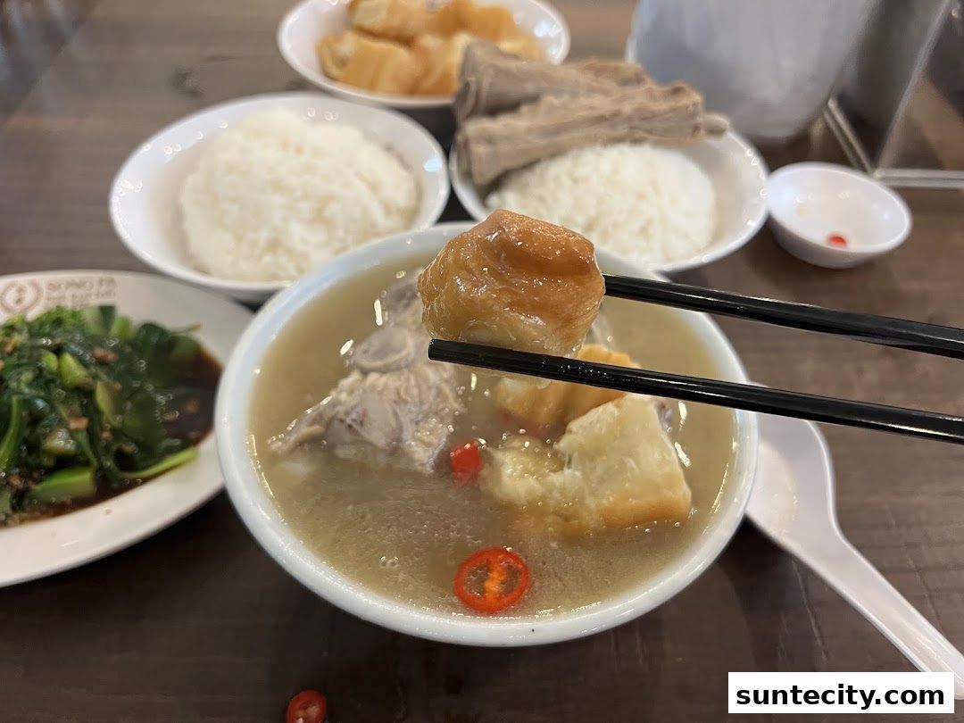 A close-up of a bowl of Bak Kut Teh with chopsticks holding a piece of dough fritter.