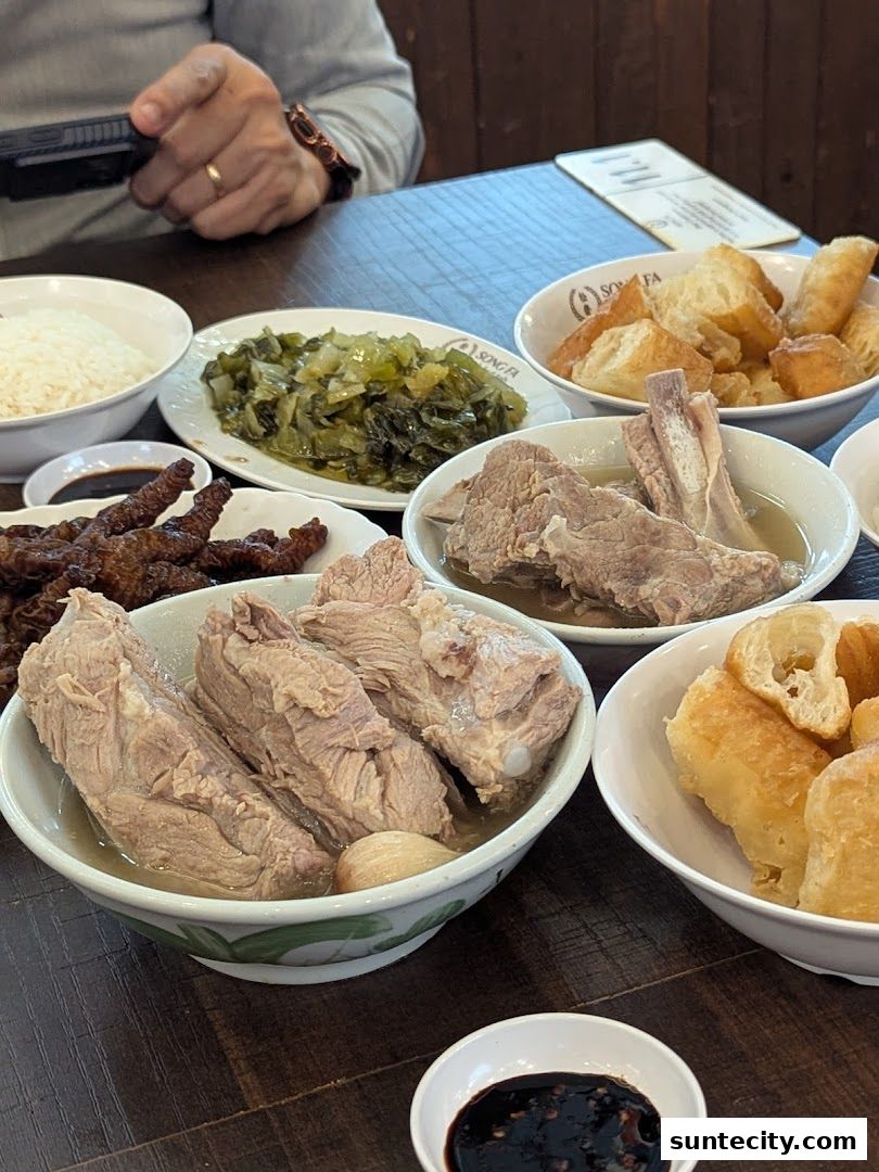A table laden with Song Fa Bak Kut Teh dishes, including pork ribs, preserved vegetables, and fried dough fritters.