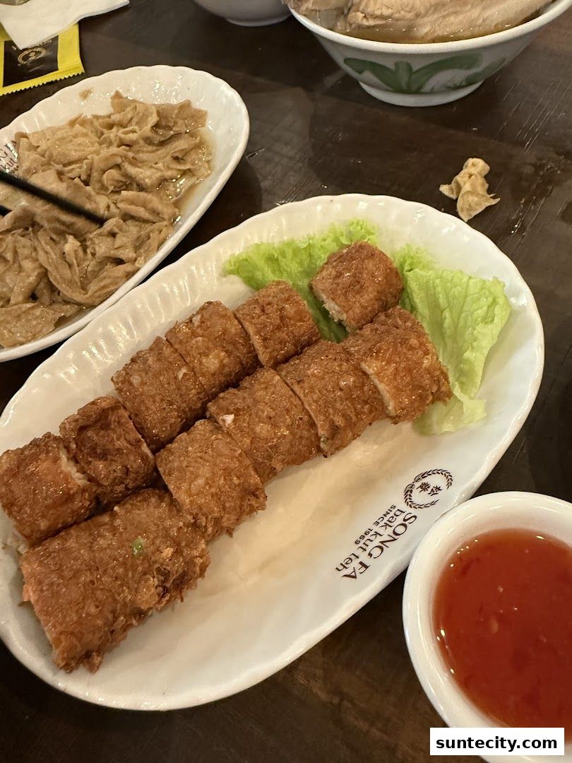 A plate of fried spring rolls with a side of dipping sauce and braised tofu skin.