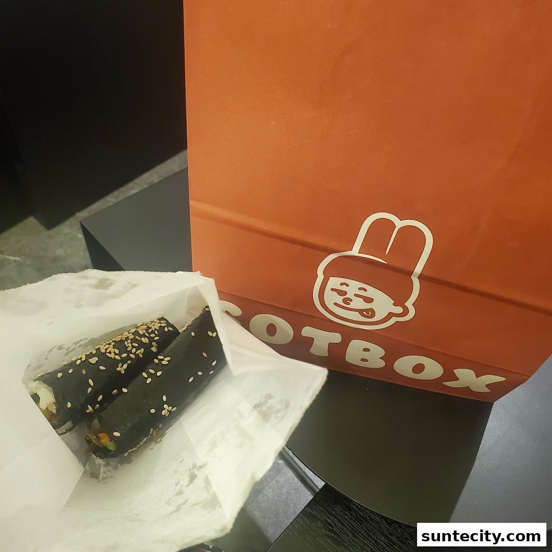 A paper bag from Sotbox contains two sushi rolls with sesame seeds.
