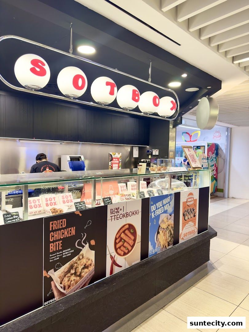 A food stall named SOTBOX with illuminated letters and posters of Korean fried chicken and tteokbokki.
