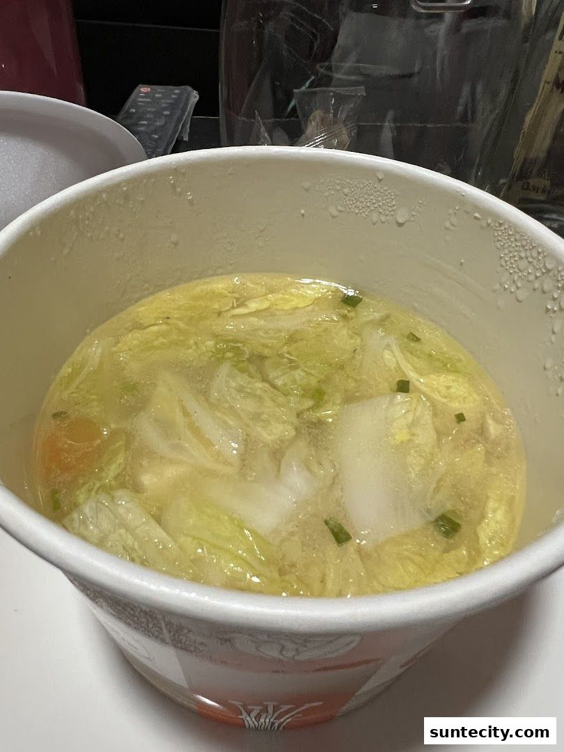 A close-up of a steaming cup of vegetable soup with napa cabbage and carrots.