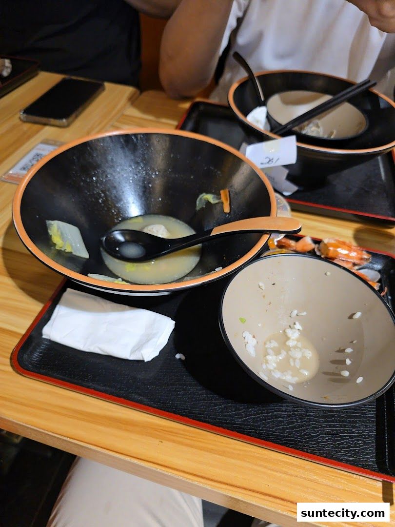 Two nearly empty soup bowls with chopsticks and a napkin on a wooden table.