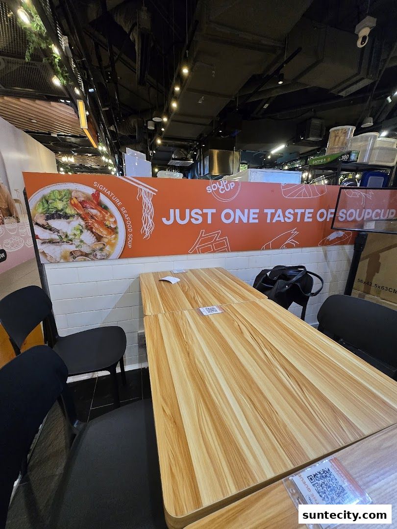 A table and chairs inside SoupCup Suntec City with a large orange banner advertising signature seafood soup.