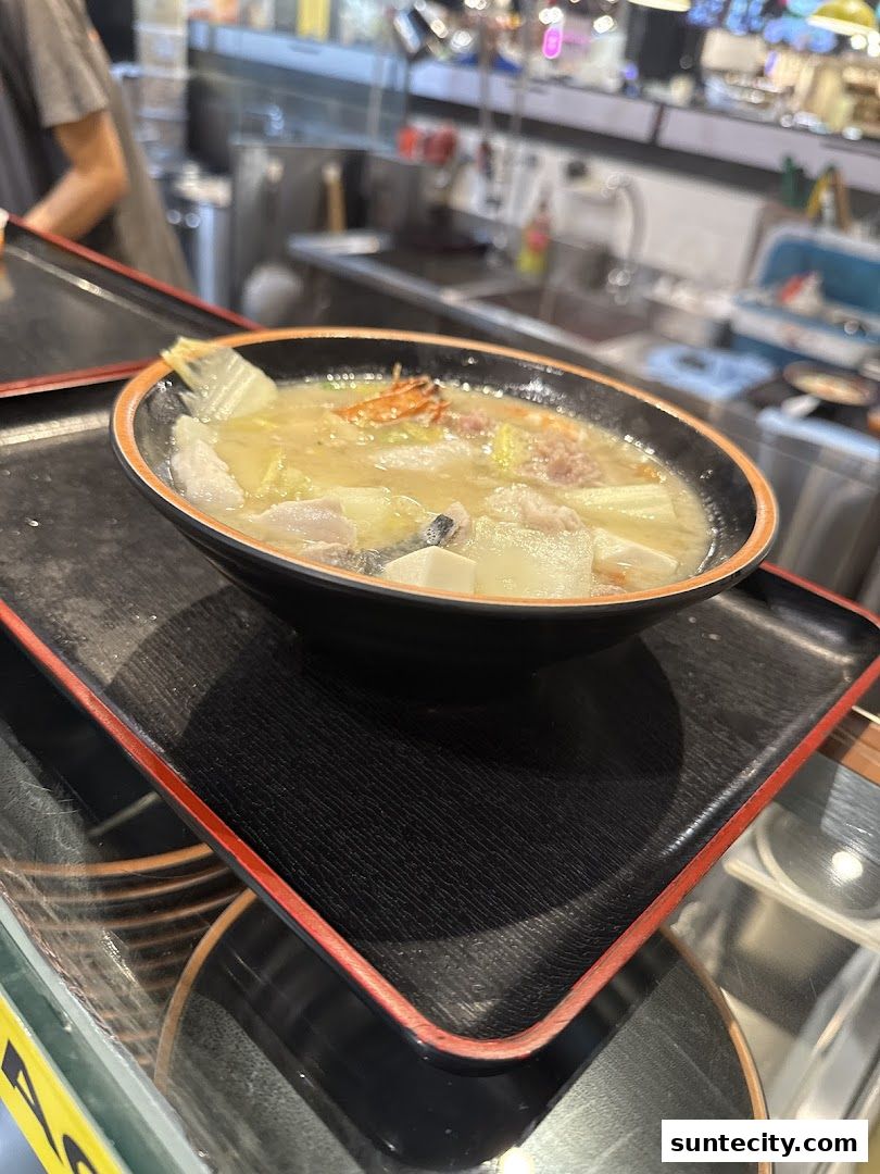 A steaming bowl of soup with various ingredients is presented on a black tray.
