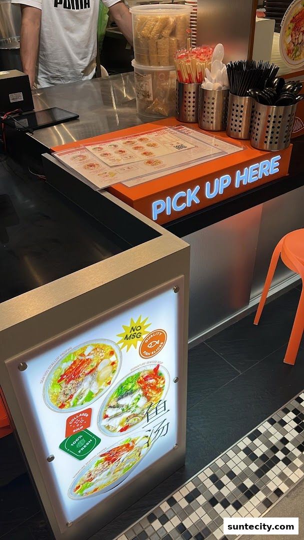 A counter at SoupCup Suntec City with a 'Pick Up Here' sign and illuminated menu display.