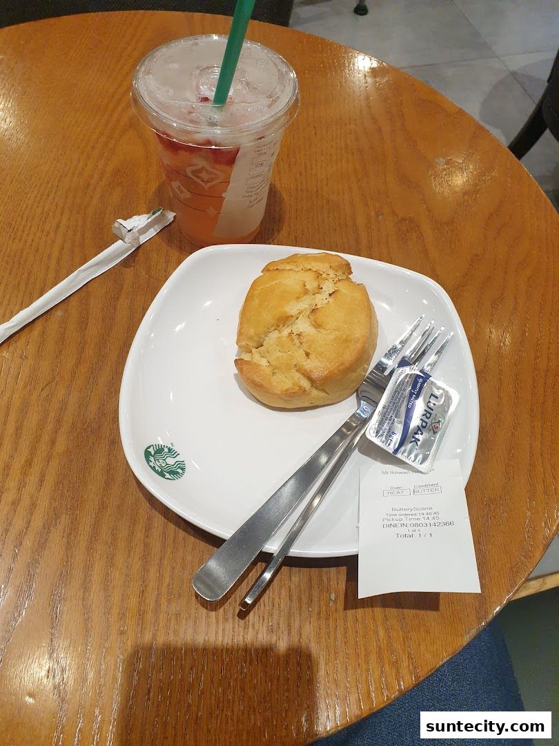 A Starbucks drink and a scone with butter on a wooden table.