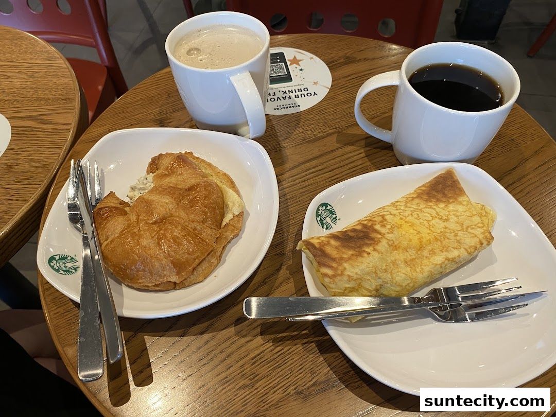 Two cups of coffee and two pastries served on plates with cutlery on a wooden table.
