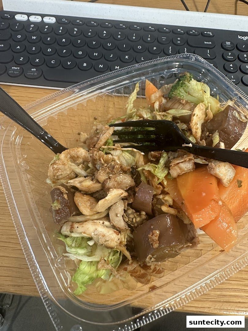 A clear plastic container filled with a salad containing chicken, lettuce, carrots, and broccoli.