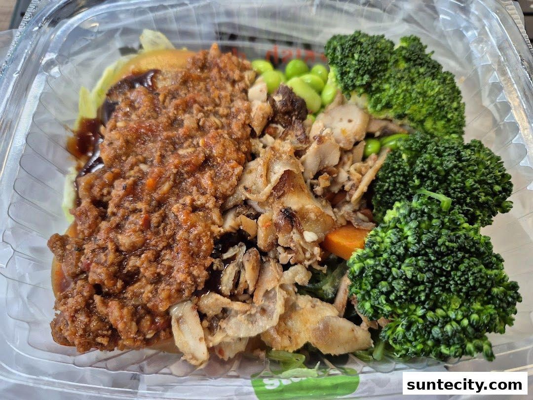 A close-up of a healthy and delicious takeaway meal with chicken, broccoli, edamame, and a savory topping.