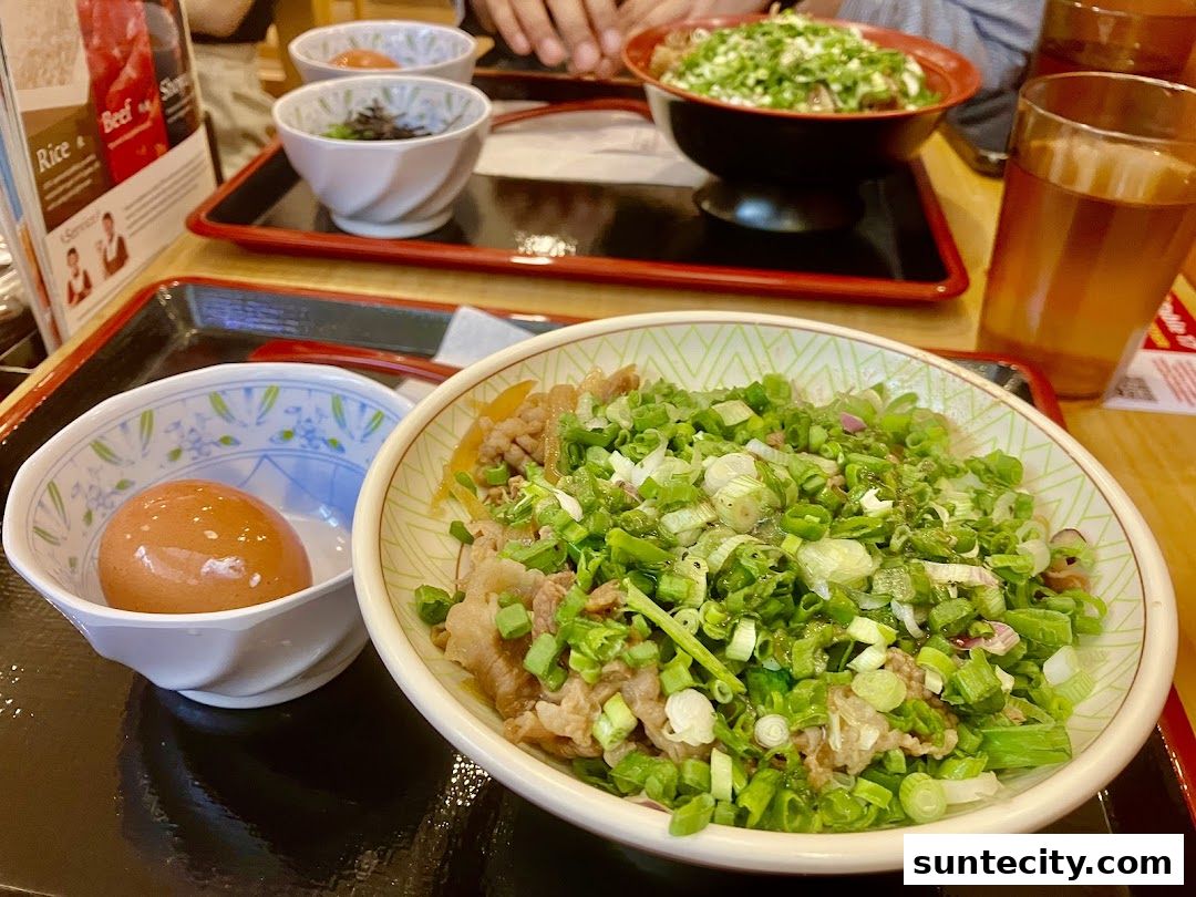A close-up of a Sukiya Gyudon dish with a side of egg and a drink.