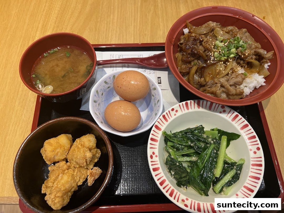 A tray of Japanese food including gyudon, miso soup, fried chicken, boiled eggs, and greens.