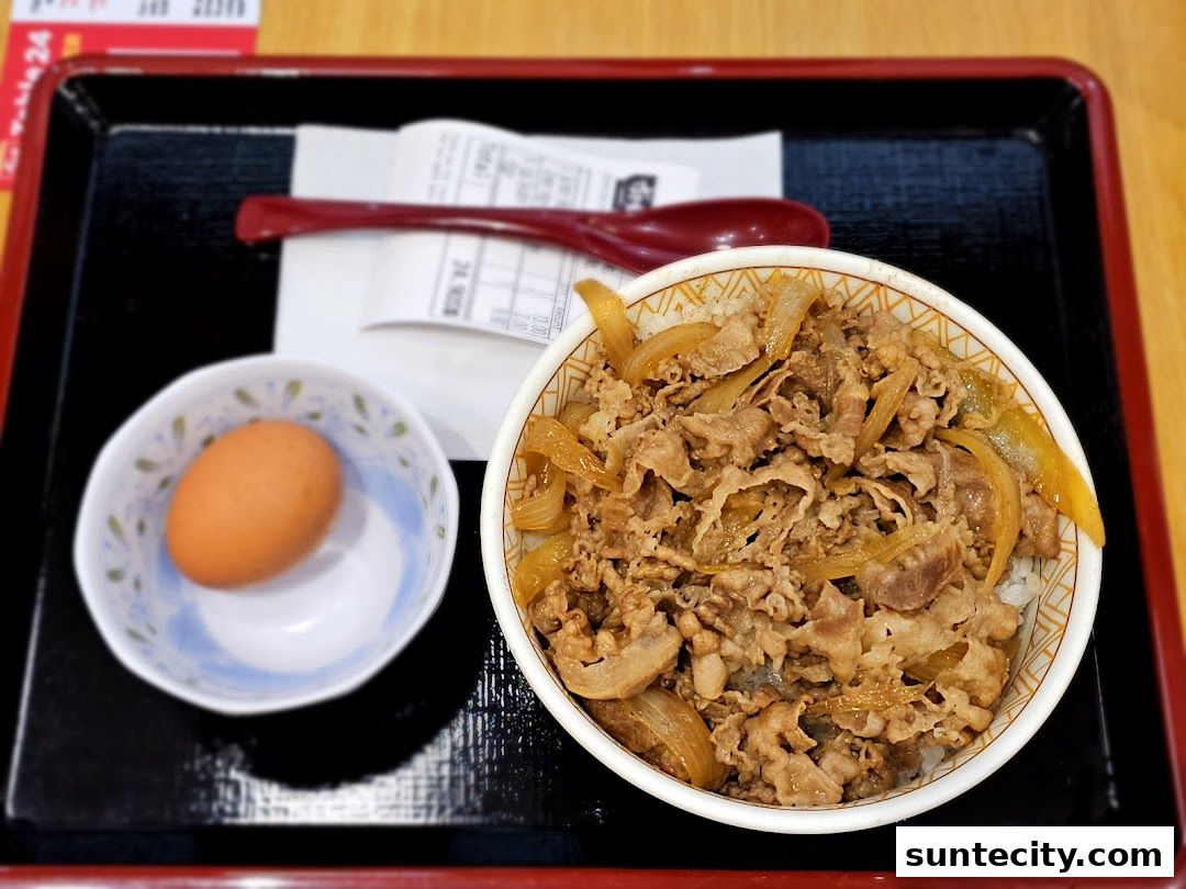 A bowl of gyudon with a side of raw egg and a receipt on a tray.