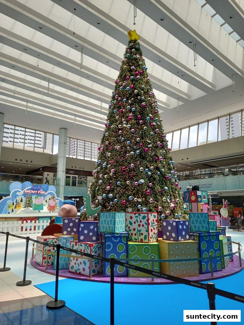 A large, decorated Christmas tree with presents and festive displays in a shopping mall.