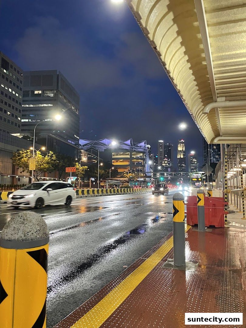 A wet city street at night with cars and buildings, viewed from a covered walkway.