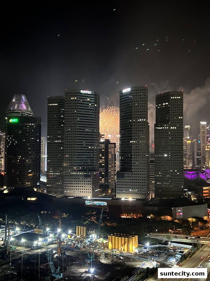 Night view of Suntec City buildings with fireworks in the background and a construction site below.