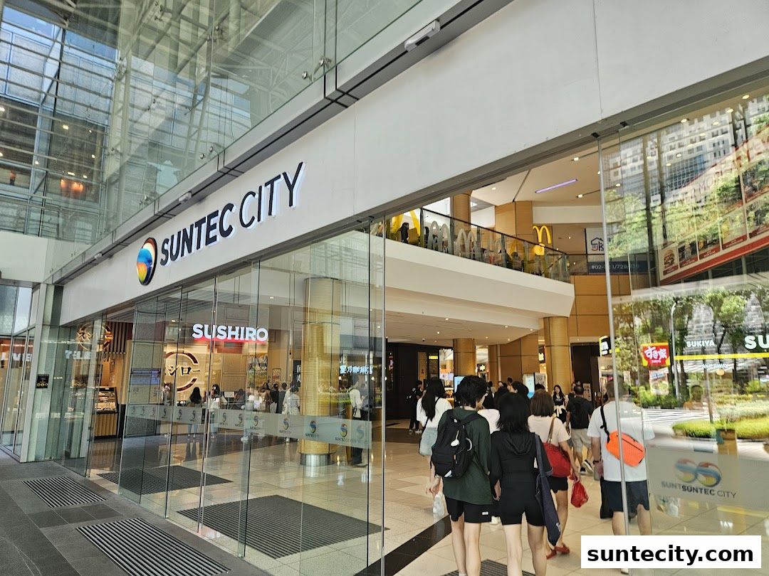 People walking past the Suntec City entrance with various shops visible inside.
