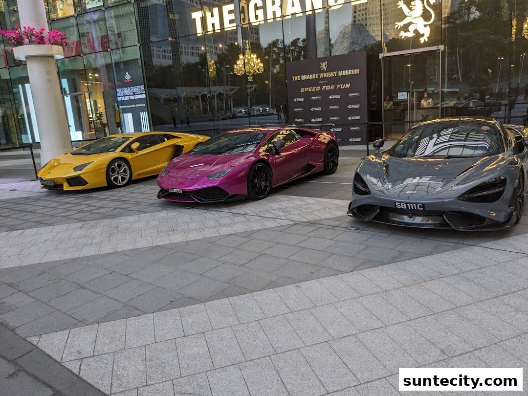 Three luxury sports cars are parked outside a building with a large glass facade.
