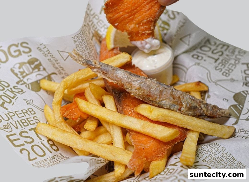 A basket of crispy fries, salmon pieces, and a whole fried fish with dipping sauce.