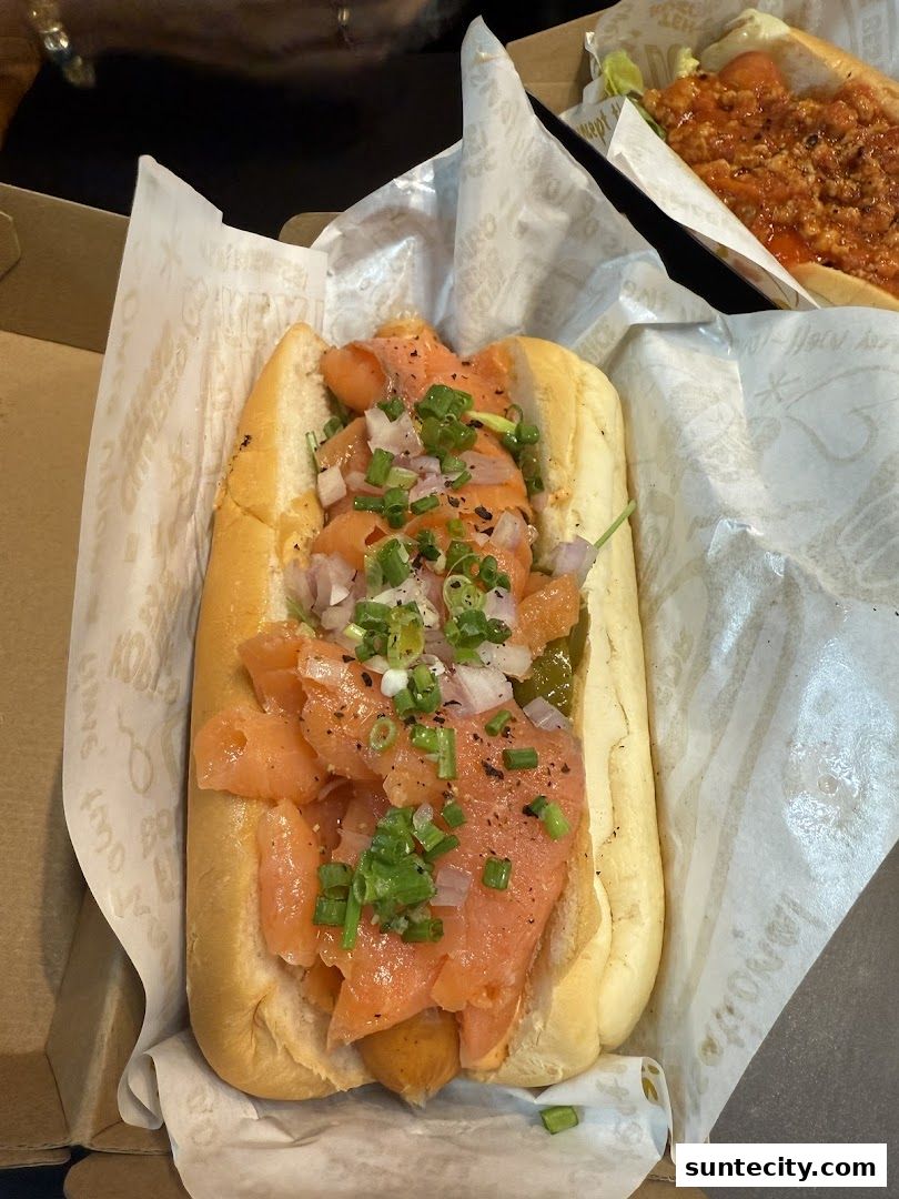 A close-up of a gourmet hot dog topped with smoked salmon, onions, and chives.