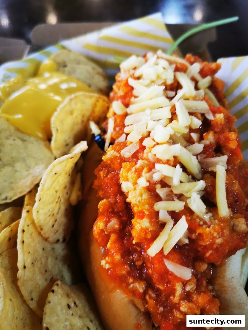 A close-up of a hot dog topped with chili and cheese, served with tortilla chips and cheese sauce.