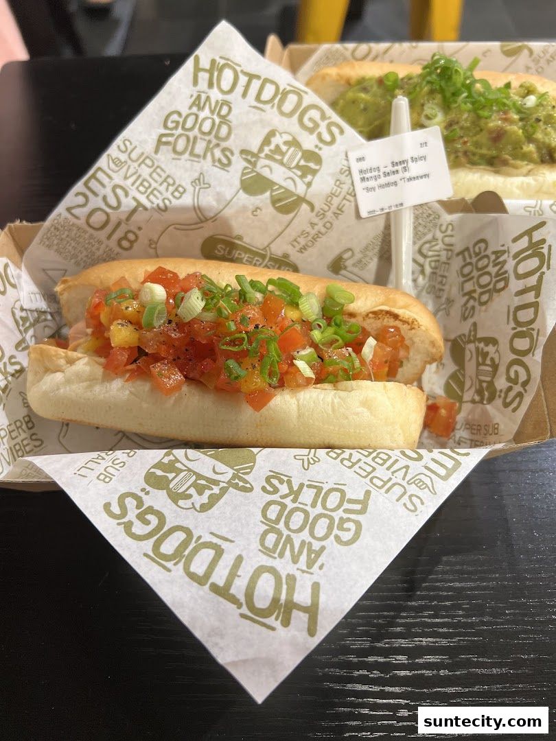 Two gourmet hotdogs with fresh toppings, served on branded paper.