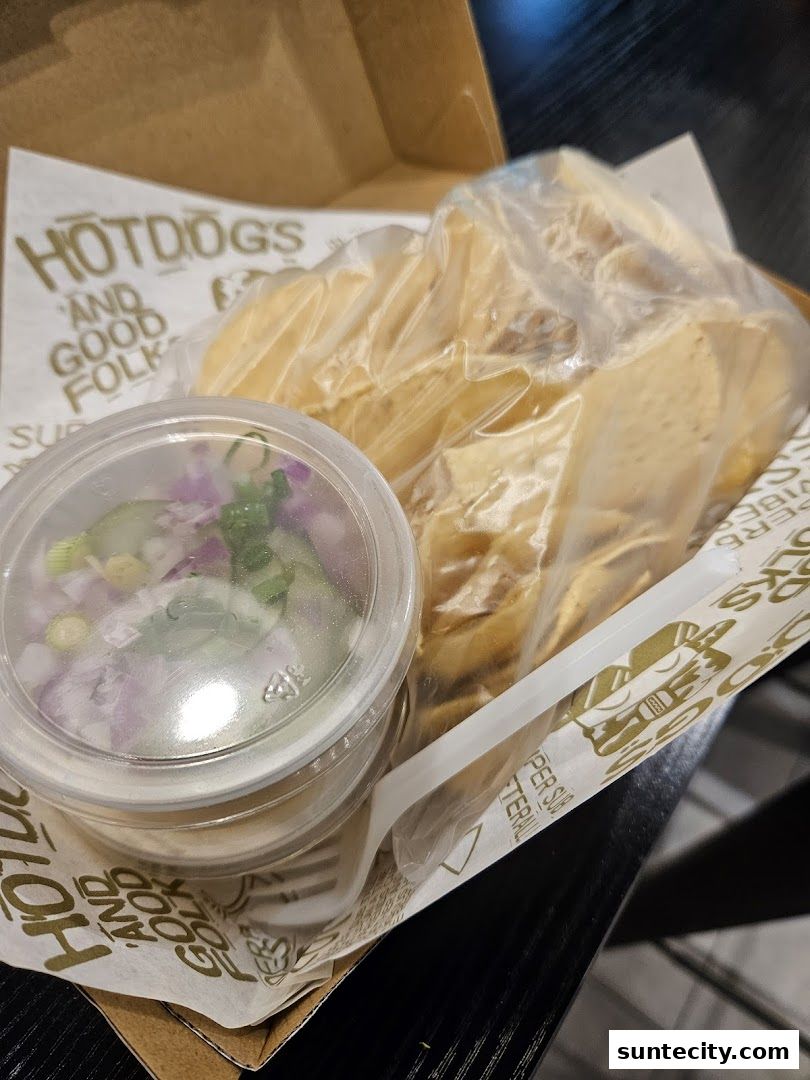 A box of hot dogs and chips with a side of salsa.