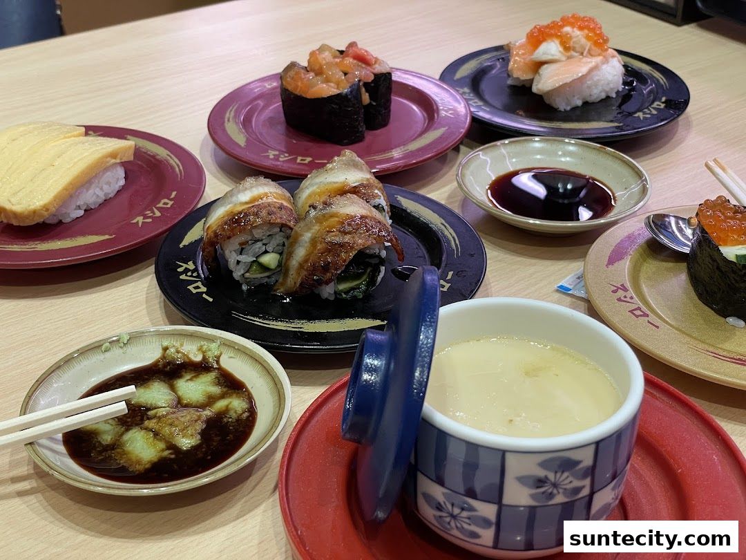 A variety of sushi dishes and a steamed egg custard are arranged on a wooden table.