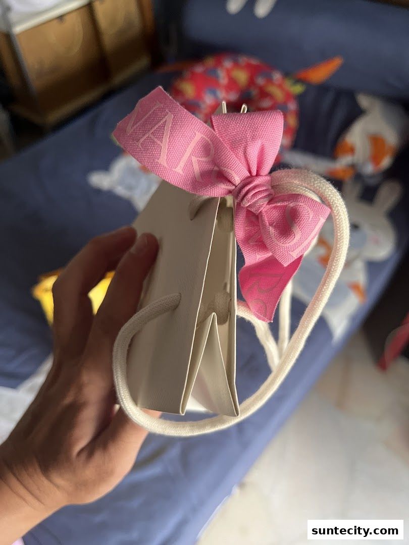 A hand holds a small white gift bag with a pink ribbon tied in a bow.