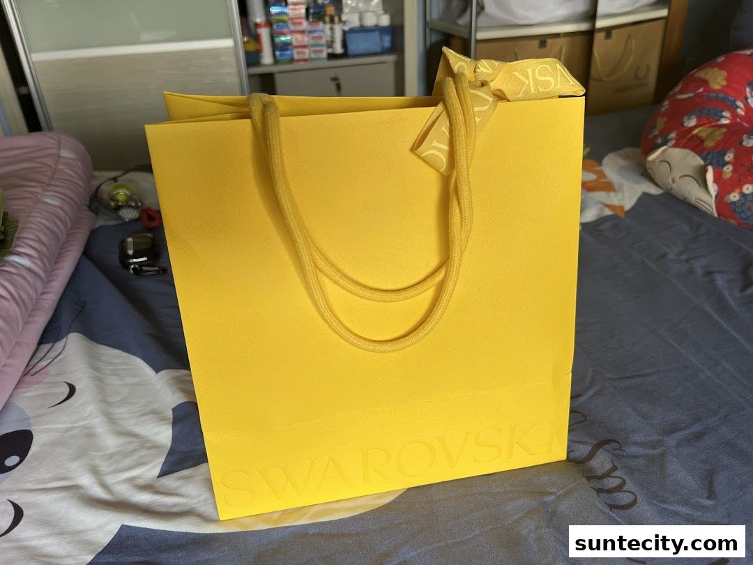 A bright yellow shopping bag from Swarovski with its logo embossed on the front.