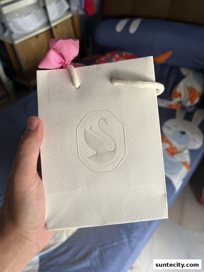 A hand holds a white Swarovski shopping bag with a pink bow.