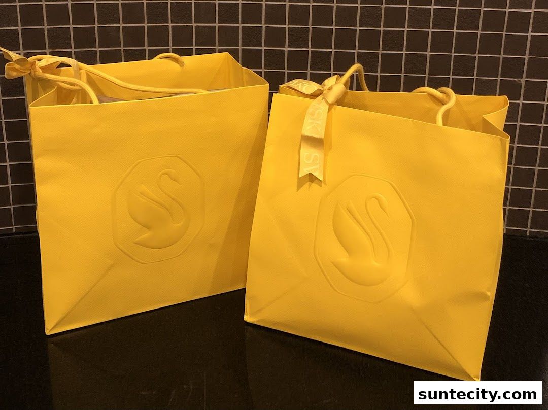 Two bright yellow shopping bags with the Swarovski swan logo embossed on them.
