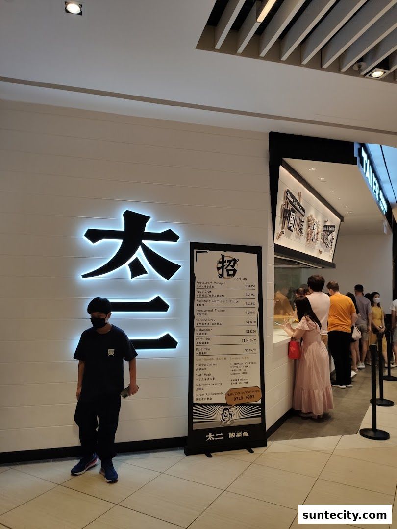 A person stands in front of the illuminated Tai Er Suntec shop front with a recruitment banner.