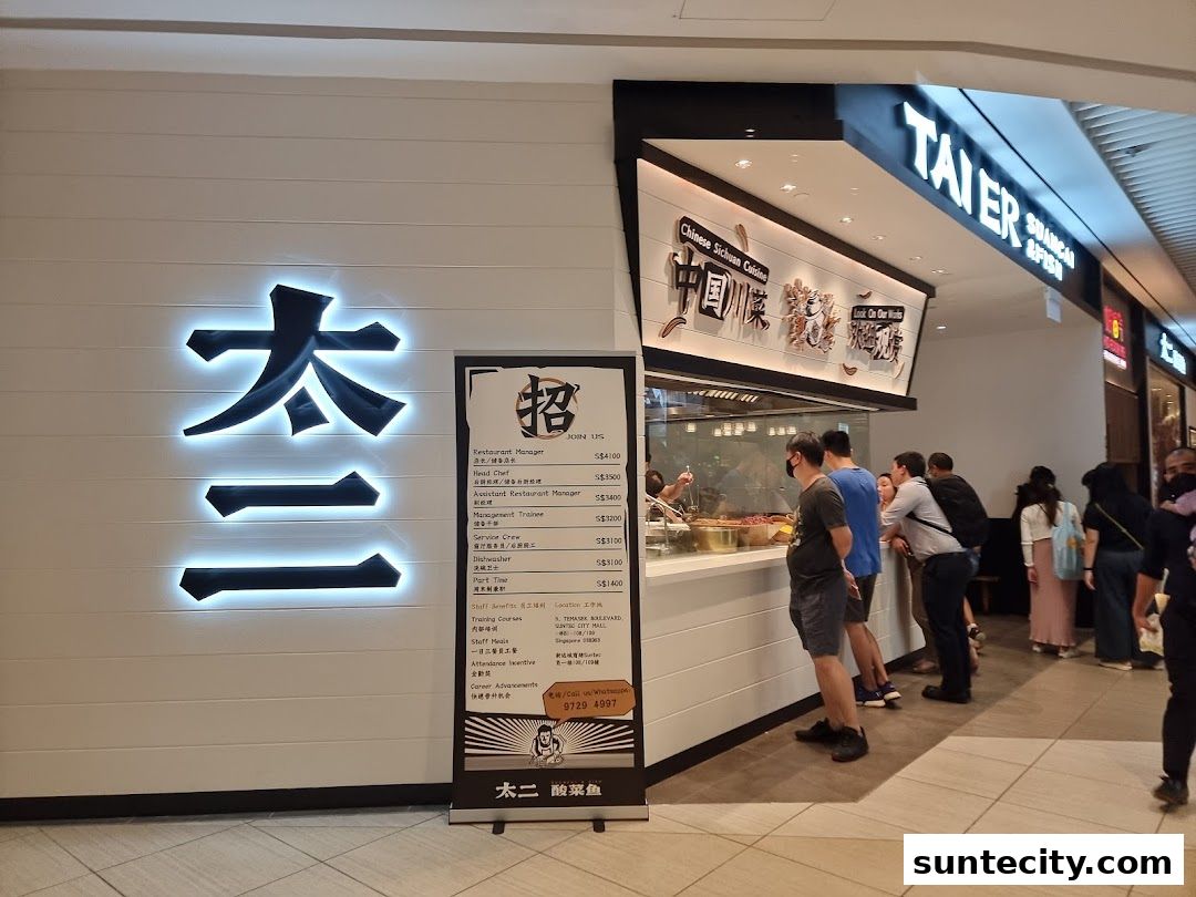 The exterior of a Chinese Sichuan Cuisine restaurant called Tai Er, with a queue of customers.