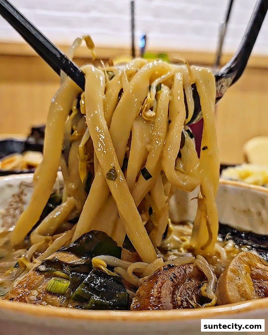 A close-up shot of thick udon noodles being lifted with chopsticks from a bowl of soup.