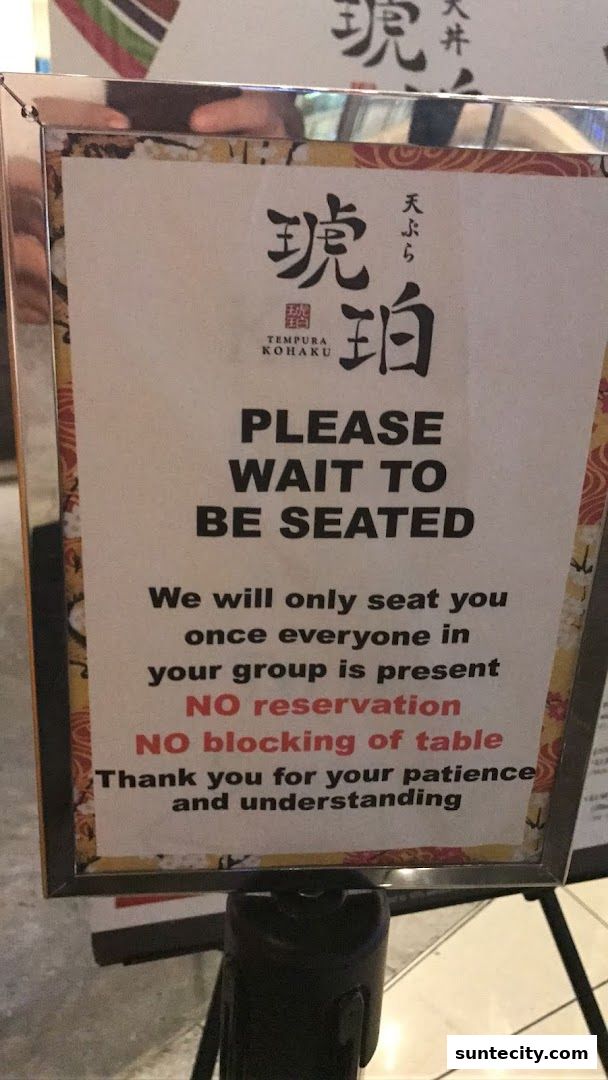 A sign at Tendon Kohaku Tempura restaurant stating 'Please Wait To Be Seated'.