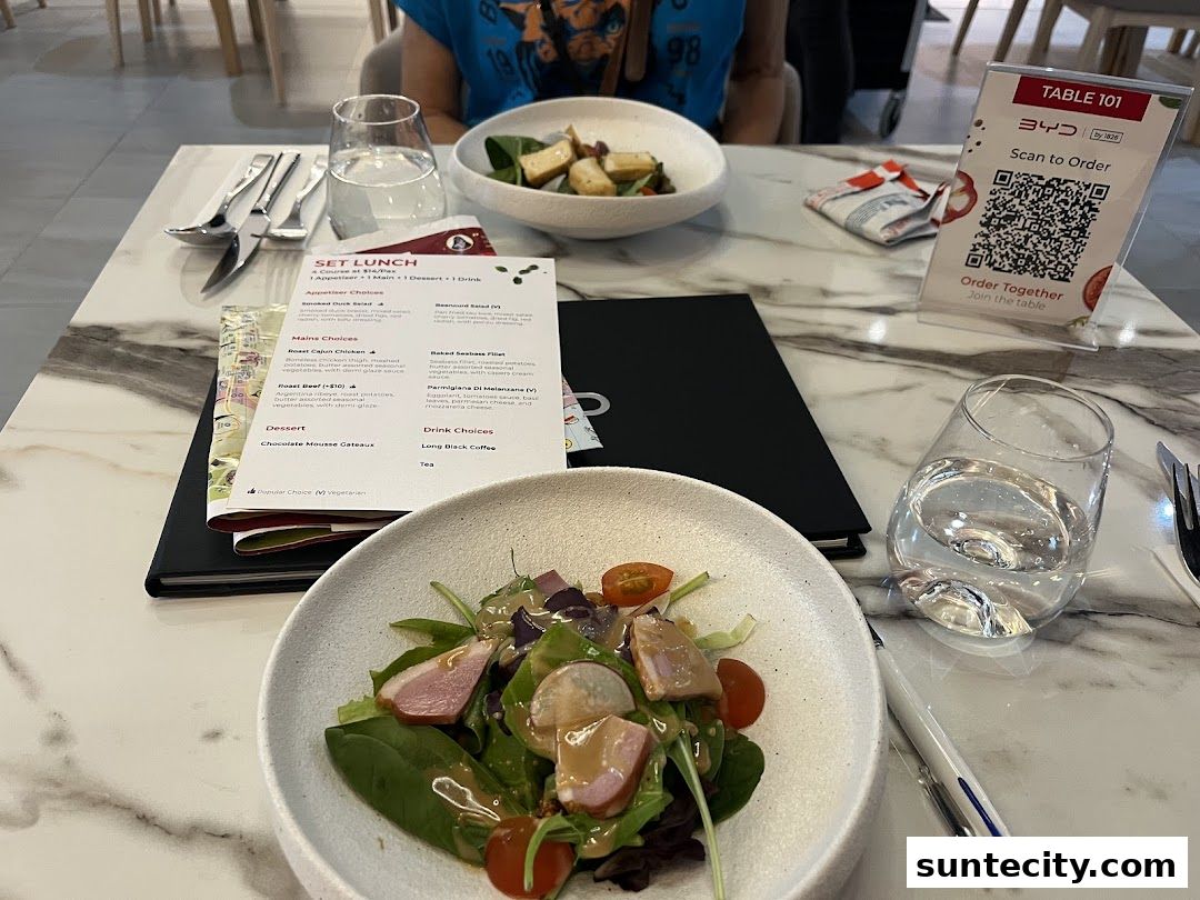 A table setting with two salads, drinks, and a set lunch menu.