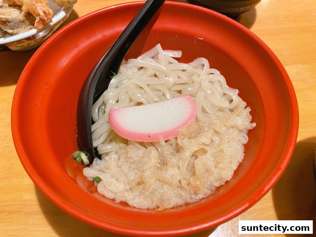 A close-up of a bowl of udon noodles with tempura and a slice of fish cake.