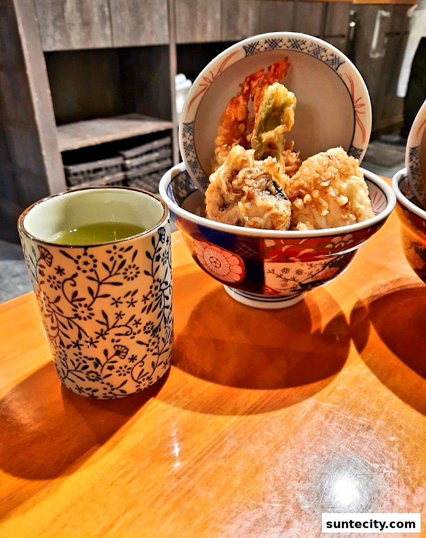A close-up of a Japanese tempura rice bowl with a cup of green tea.