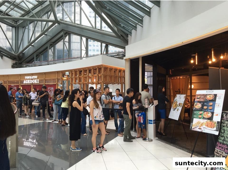 A long queue of people waiting outside a Japanese restaurant with menu boards displayed.