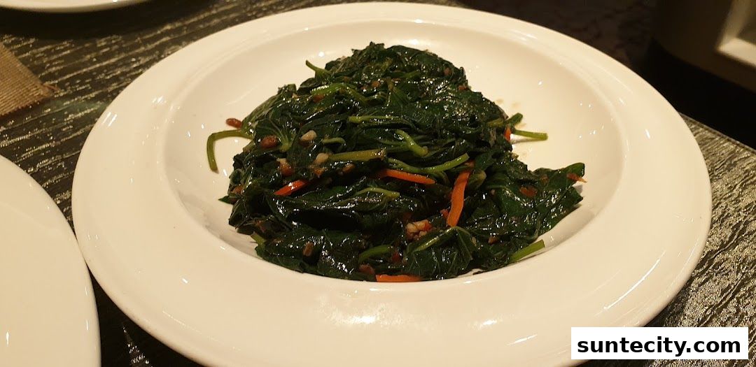 A close-up shot of a white bowl filled with stir-fried leafy green vegetables and julienned carrots.