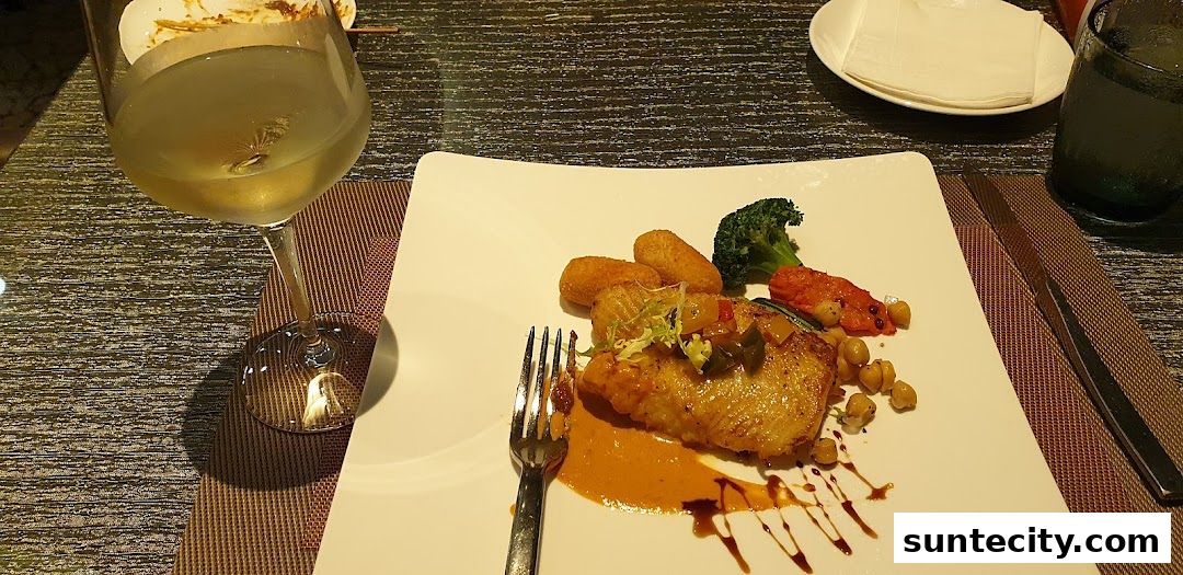 A beautifully plated dish of fish with sides and a glass of white wine.