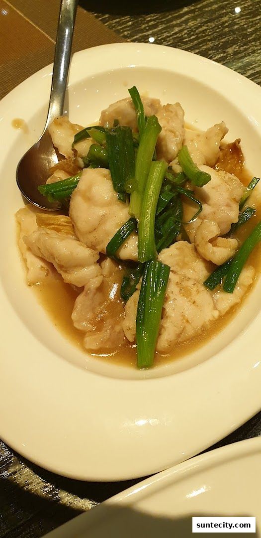 A close-up shot of a white bowl filled with fish and green onions in a savory sauce.