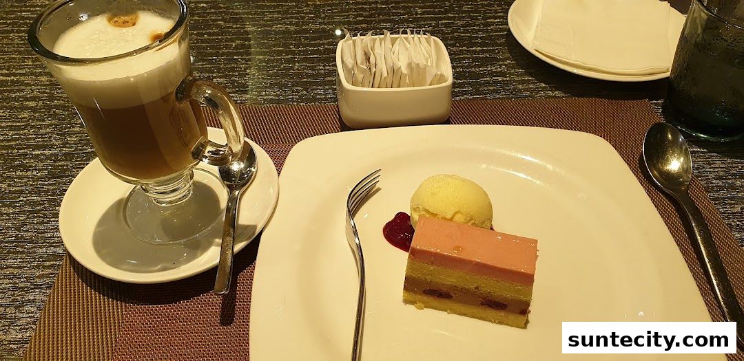 A slice of layered cake with ice cream and a coffee drink on a table.