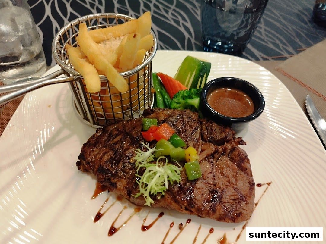 A juicy steak served with fries, vegetables, and dipping sauce on a white plate.