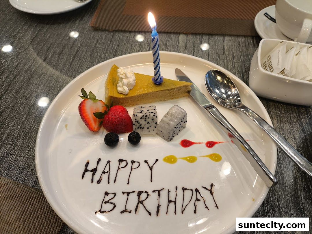 A slice of birthday cake with fruit and a lit candle on a white plate.